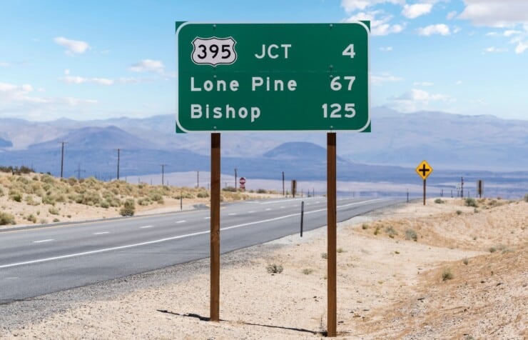 California Highway 395 road sign with empty road and mountains in background