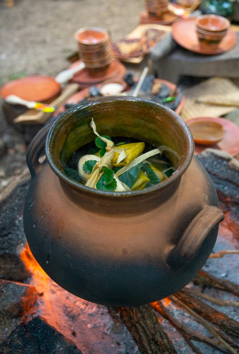 Handmade tamales cooking over a fire in a traditional earthenware cooker