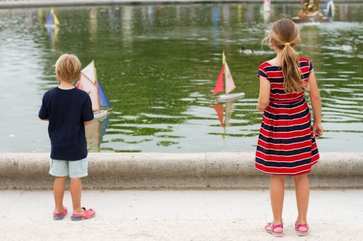 Two kids playing with toy boats on a pond in Paris
