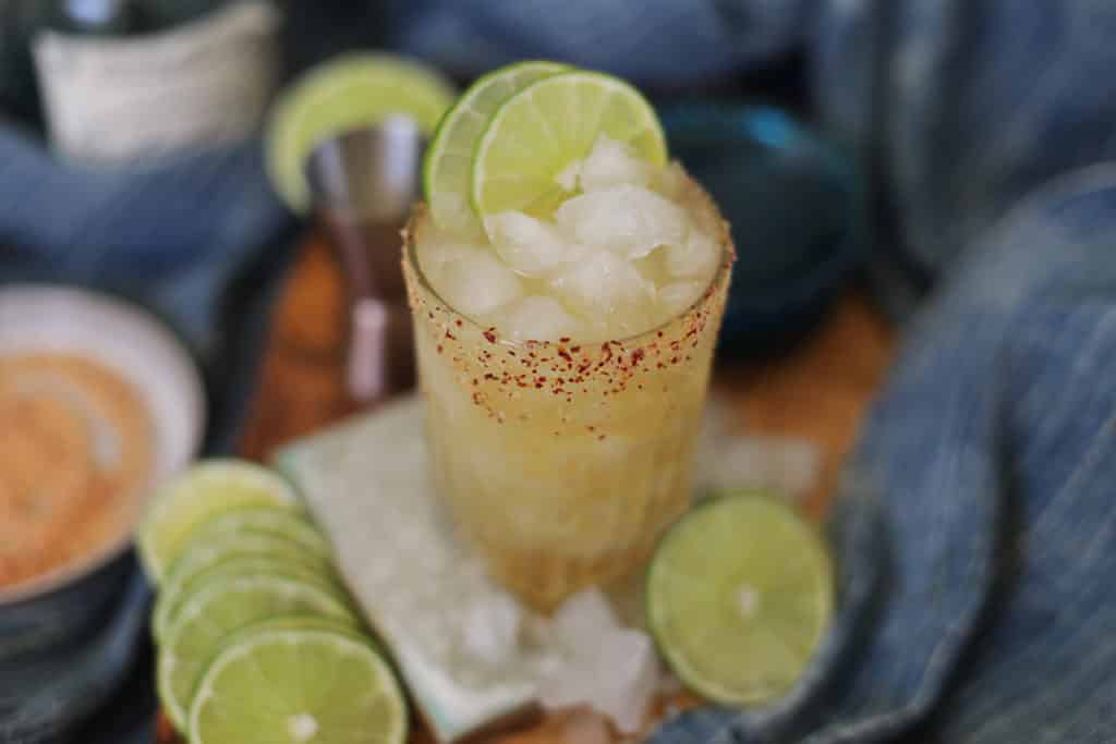 One Cadillac Margarita on a coaster with sliced limes