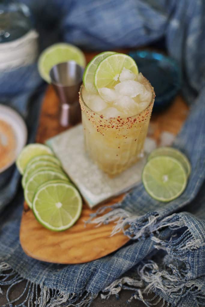 Cadillac margarita surrounded by sliced limes and a jigger