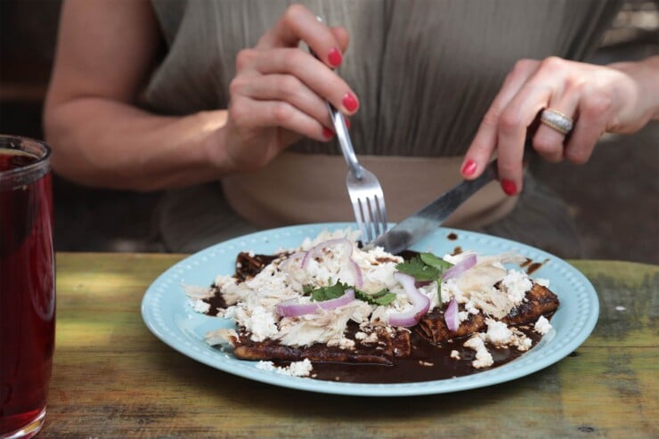 Woman cutting into a plate of traditional enmoladas mole enchiladas