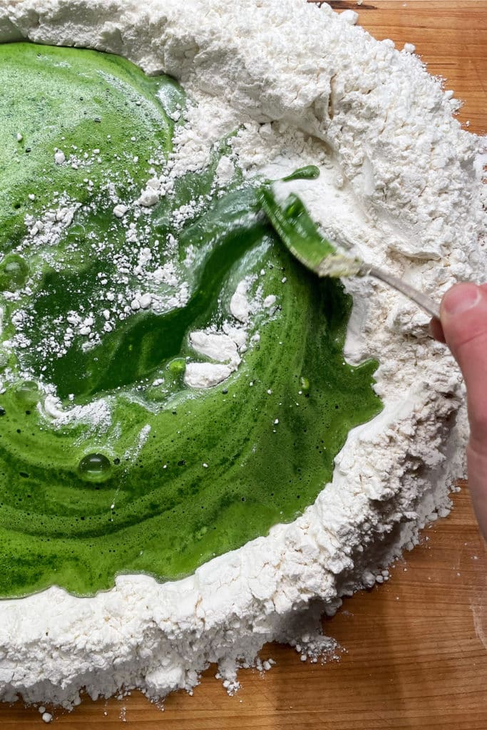 Well of flour on a cooking surface with pureed spinach for spinach pasta