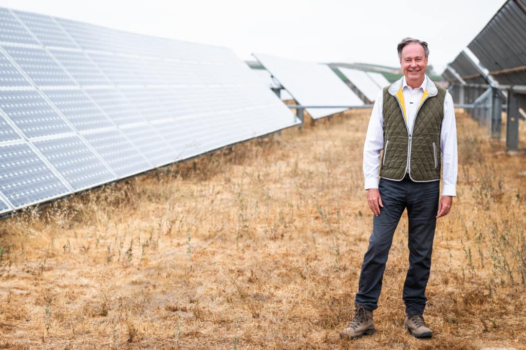 Man standing in front of solar panels in a field