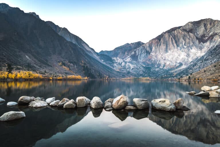 Sunrise photo of calm alpine lake with rocks in foreground