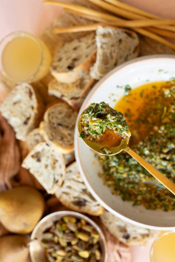 Spoon of olive dip with serving plate and appetizer spread in background