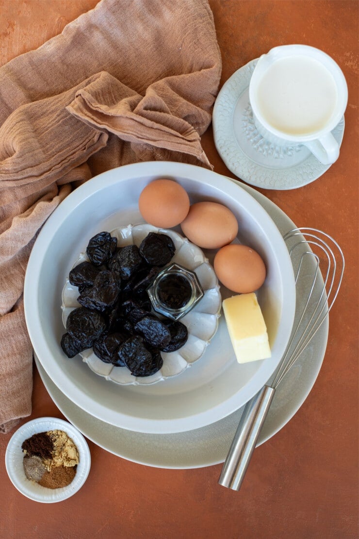 Prunes, butter, eggs, heavy cream and spices on plates with a napkin nearby