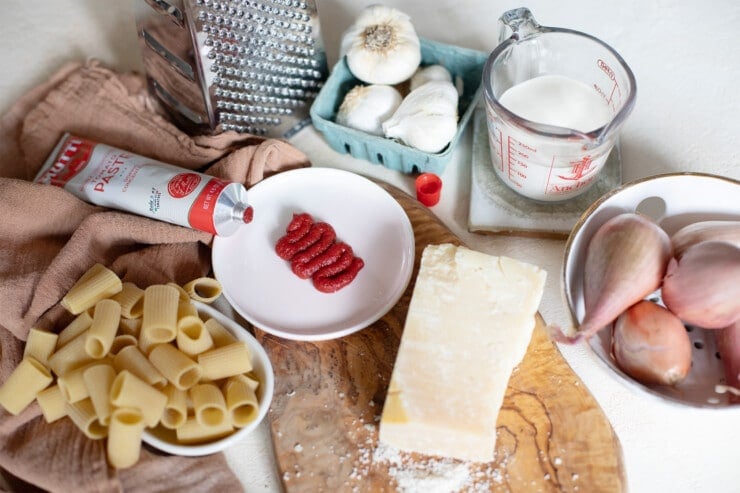 Ingredients to make spicy vodka sauce laid out on a table including mezze rigatoni, tomato paste, garlic, cream, shallots, and cheese