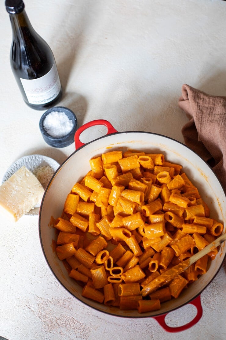 Full pot of spicy vodka sauce pasta with a bottle of red wine and cheese on the side