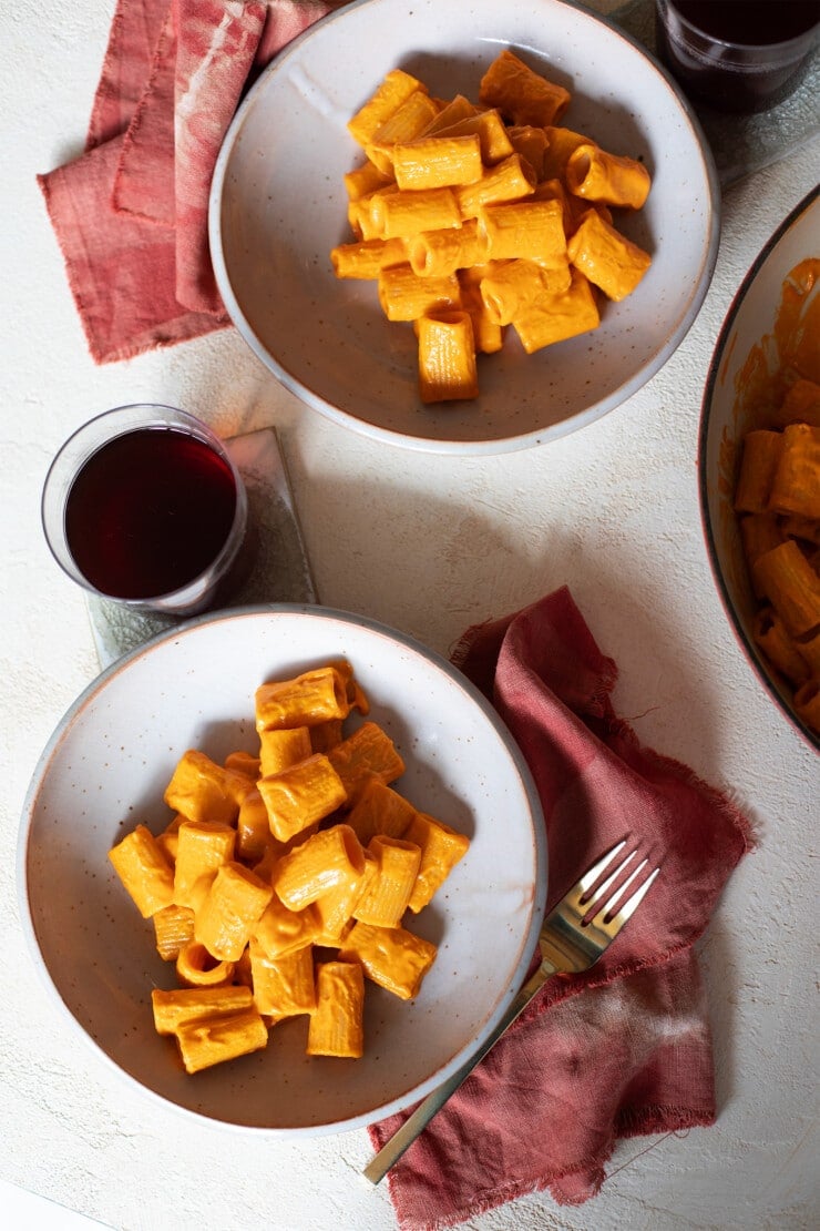 Two plates of spicy vodka sauce in bowls with forks, red wine, and napkins nearby