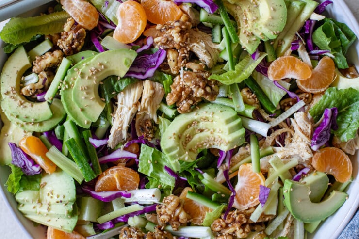 a closeup of a romaine salad with oranges, scallions, walnuts, cucumber, and avocado