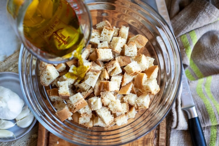 Bowl of bread cubes with oil being poured on top to make croutons