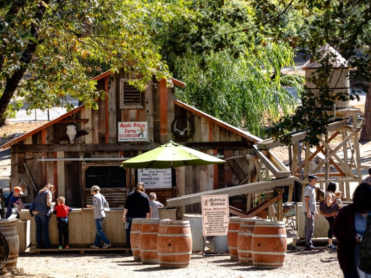 Exterior of barn with barrels, people, and trees surrounding it