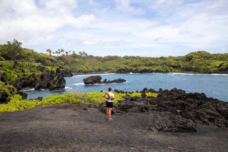 Woman on black sand cliff surrounded by naupaka and ocean