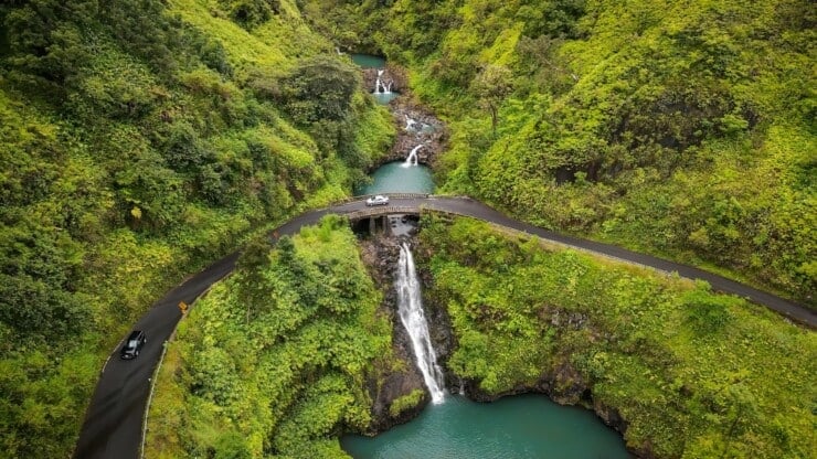 Aerial view of road over a waterfall with two cars and lush greenery