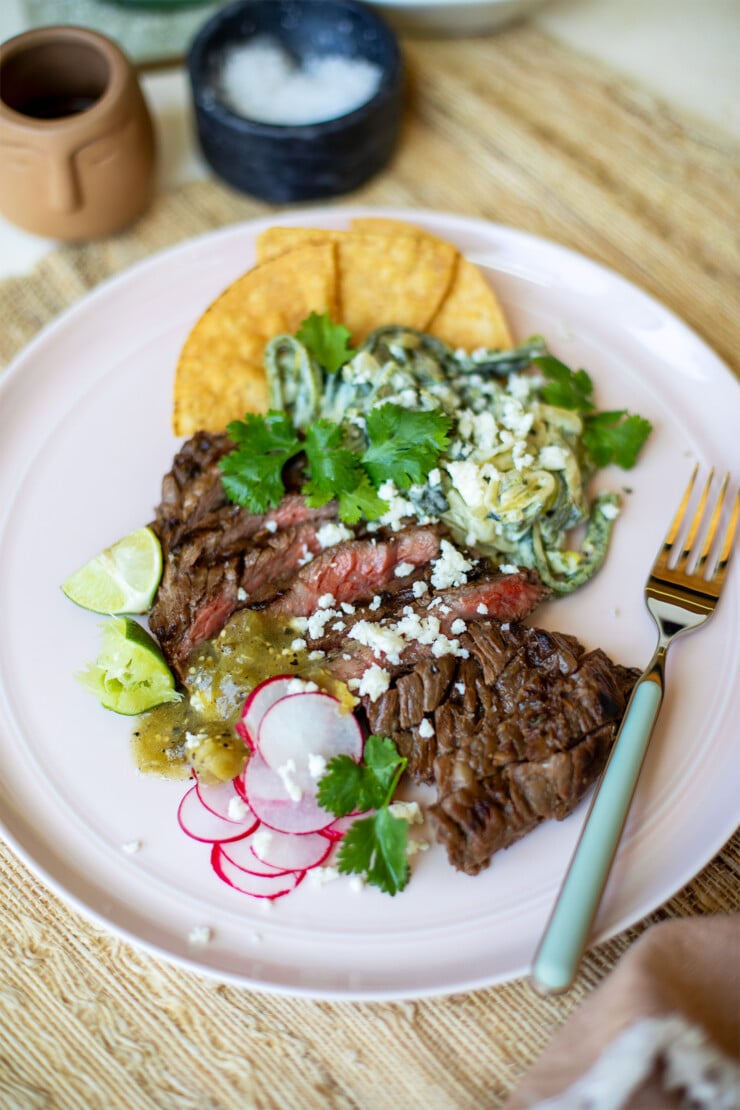 Plate with sliced steak, radishes, salsa, limes, cilantro, crumbled cheese, and tortilla chips