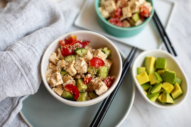 Serving dish of tofu poke with another bowl and some avocado nearby