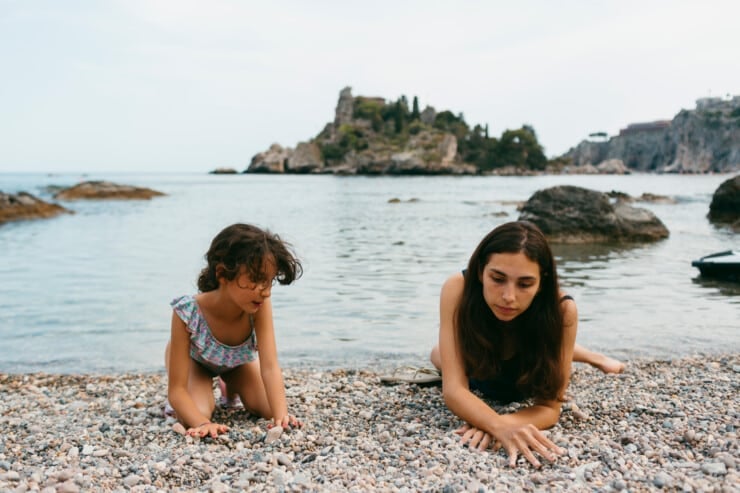 Woman and kid in swimwear on the shore of pebble beach having fun looking for pebbles in gravel beach in Isola-Bella island in SIcily, in the Mediterranean Sea