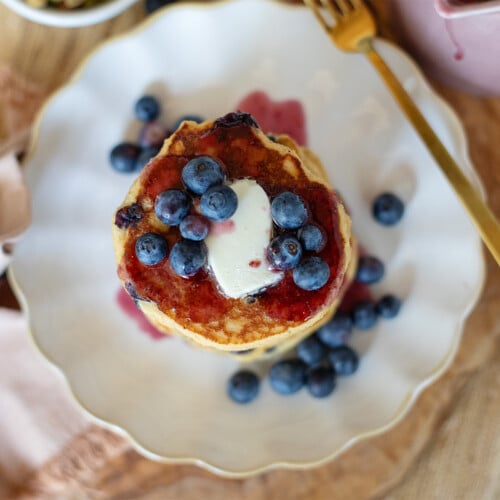 Overhead photo of a pancake with blueberries butter on a plate with a fork and napkin