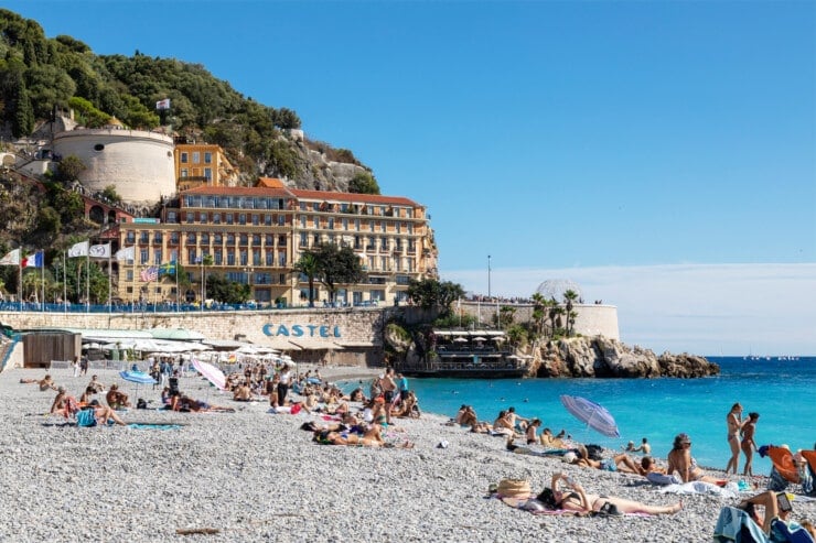 Beach with people lying on shore with beach club, hotel, and Castel hill in distance
