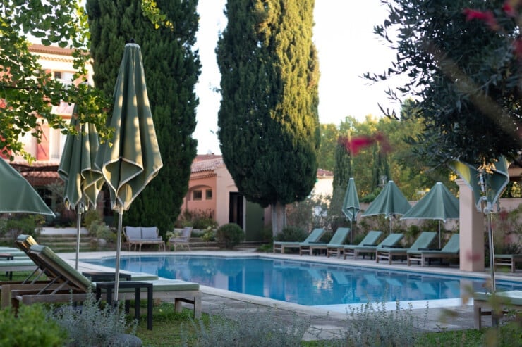Hotel pool with chaise lounges, umbrellas, and cypress trees