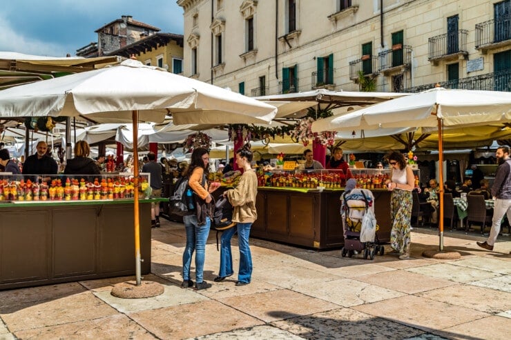 Two shoppers chatting under a market umbrella at Piazza delle Erbe in Verona