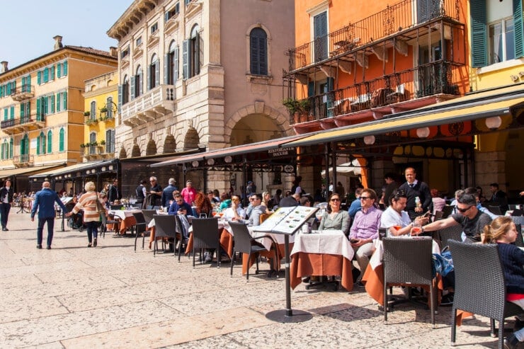 Café terraces set for lunch along a sunny Verona street