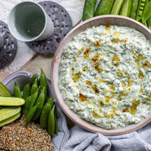Bowl of yogurt dip surrounded by snap peas, cucumbers, crackers, and water
