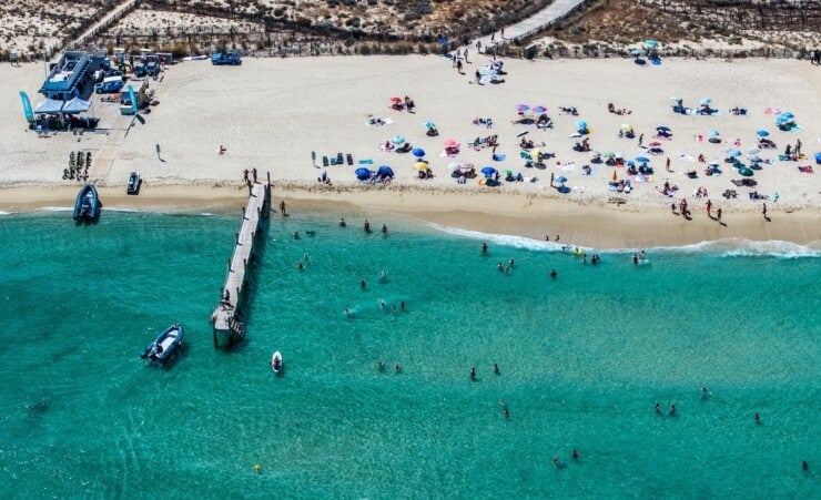 Aerial view of Pampelonne Beach with many parasols and a pier, located at coastline of Ramatuelle, Côte d’Azur, France, people sunning on the beach and playing in the water